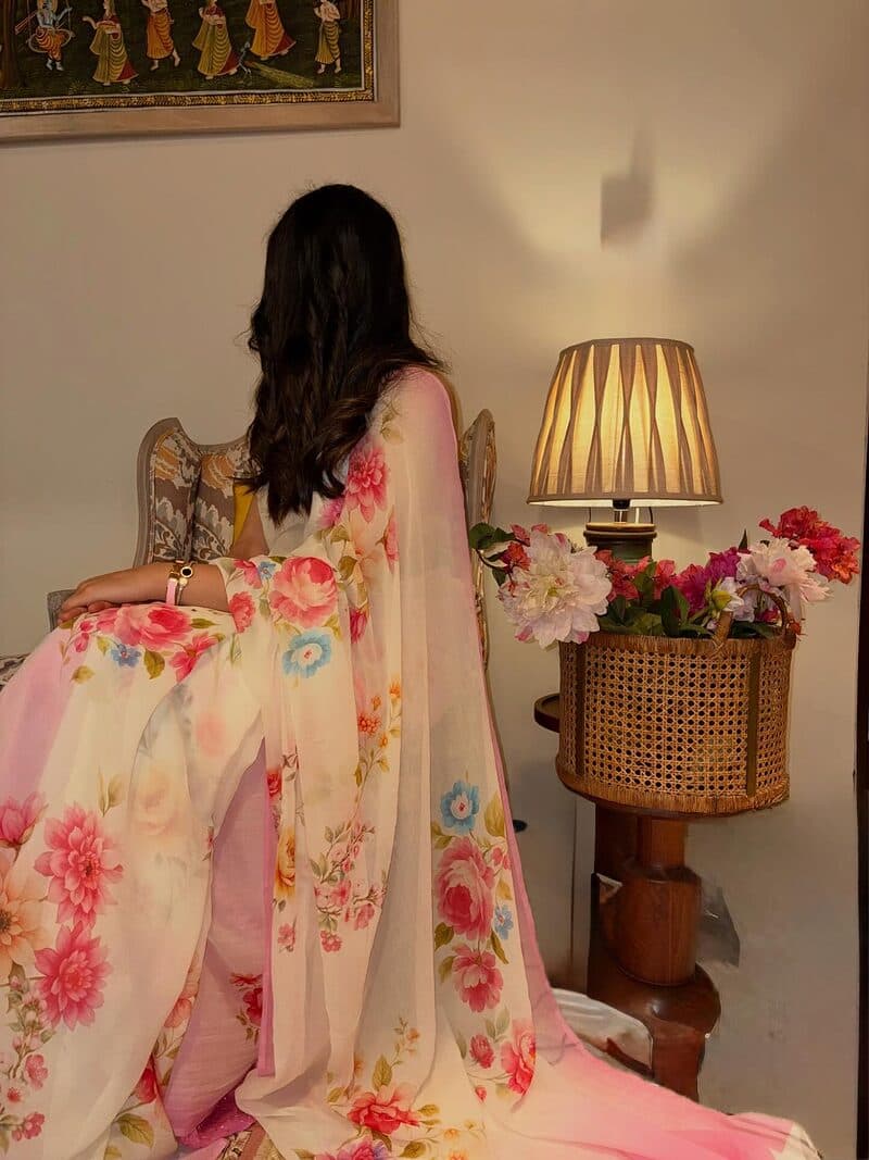A pale pink saree printed with roses, draped and worn in a lamp-lit room
